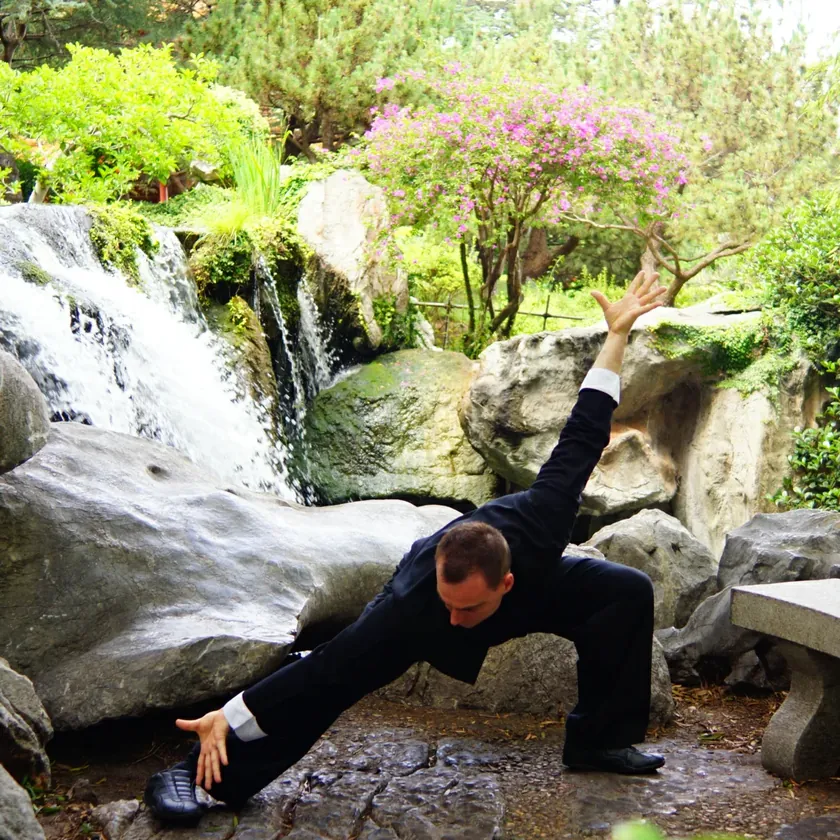 Grant Mundy holding a low Baguazhang stance in front of a garden waterfall