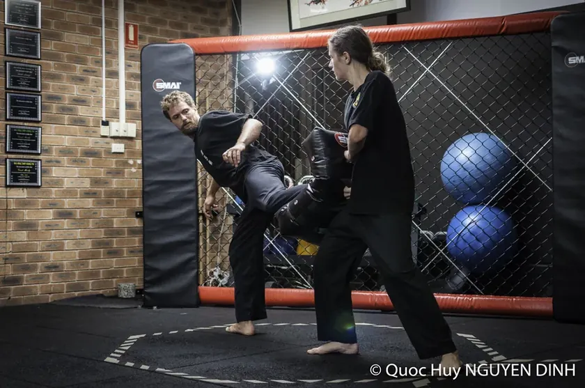 Two students working a kick pad drill in the training cage