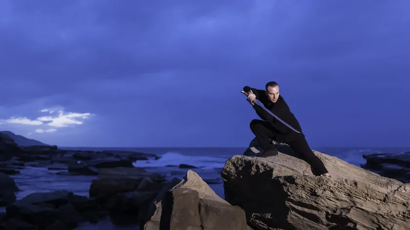 Grant Mundy crouched with a dao broadsword on the Terrigal coastline at night