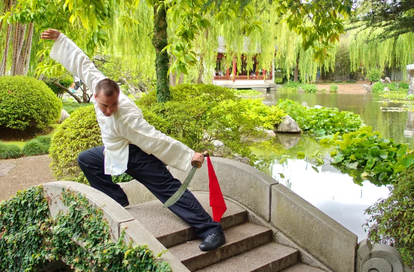 Grant Mundy practising a Tai Chi dao form beside a willow-lined pond