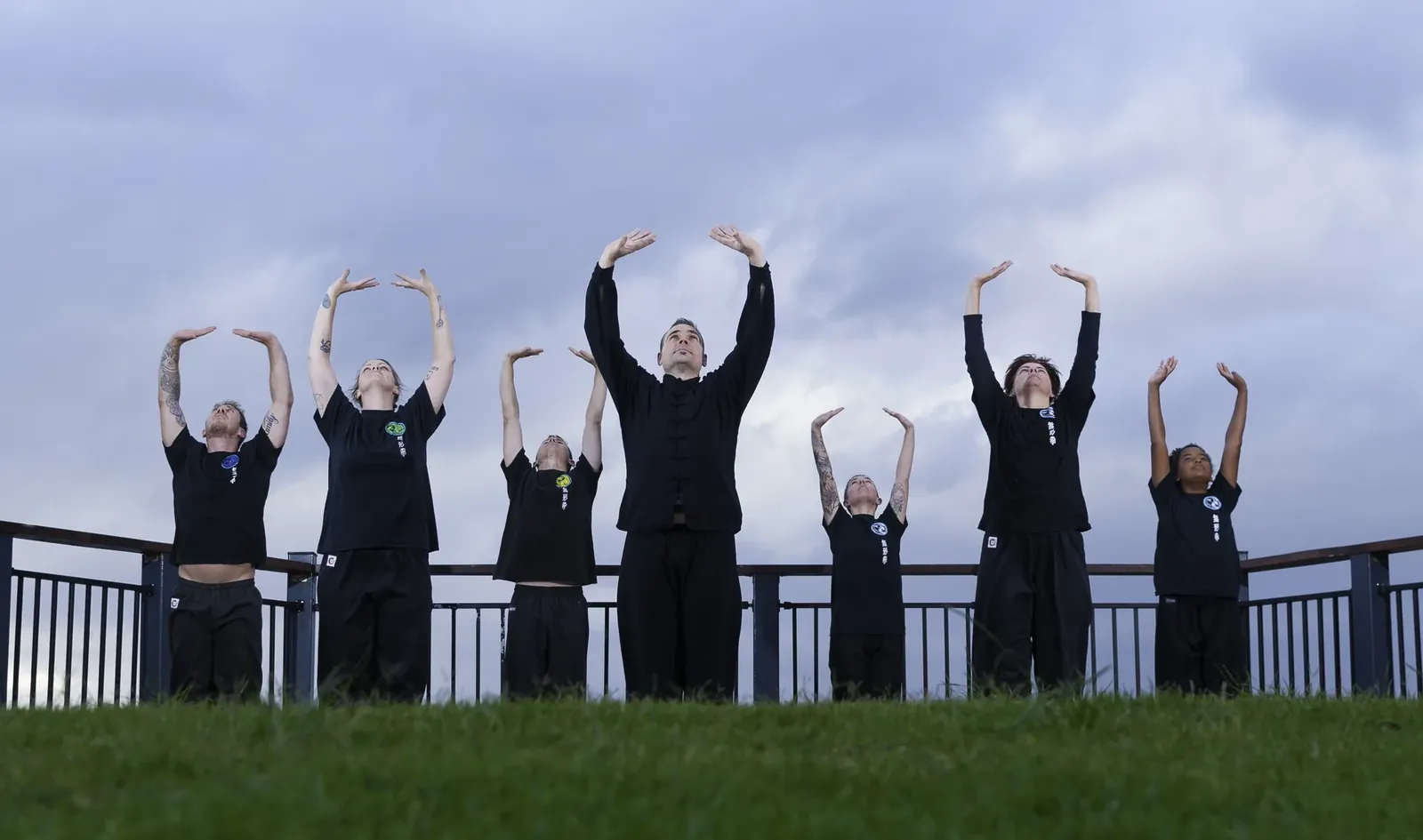 A Wu Xing Dao group practising Qigong outdoors at dusk, arms raised to the sky