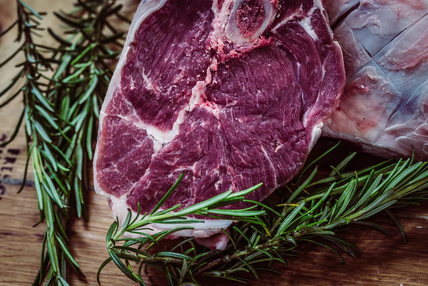 Raw marbled steak with rosemary sprigs on a wooden cutting board