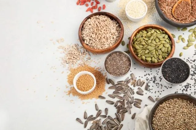 Assorted seeds and grains in wooden and metal bowls scattered on a white background, top view.