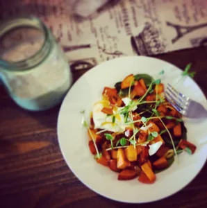 Plate of roasted vegetables topped with microgreens beside a glass jar on a rustic table.