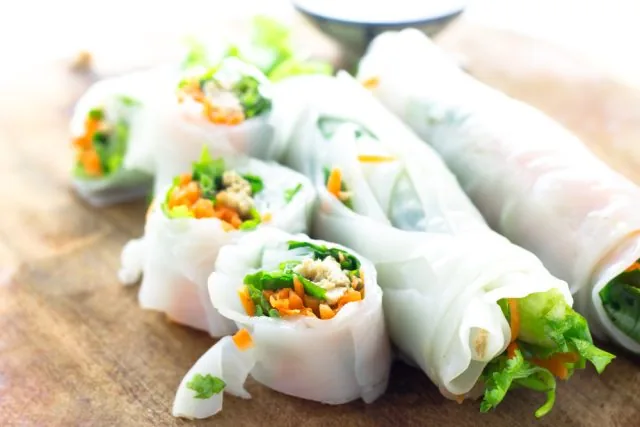 Fresh rice paper spring rolls with vegetables on a wooden board, brightly lit and appetizing