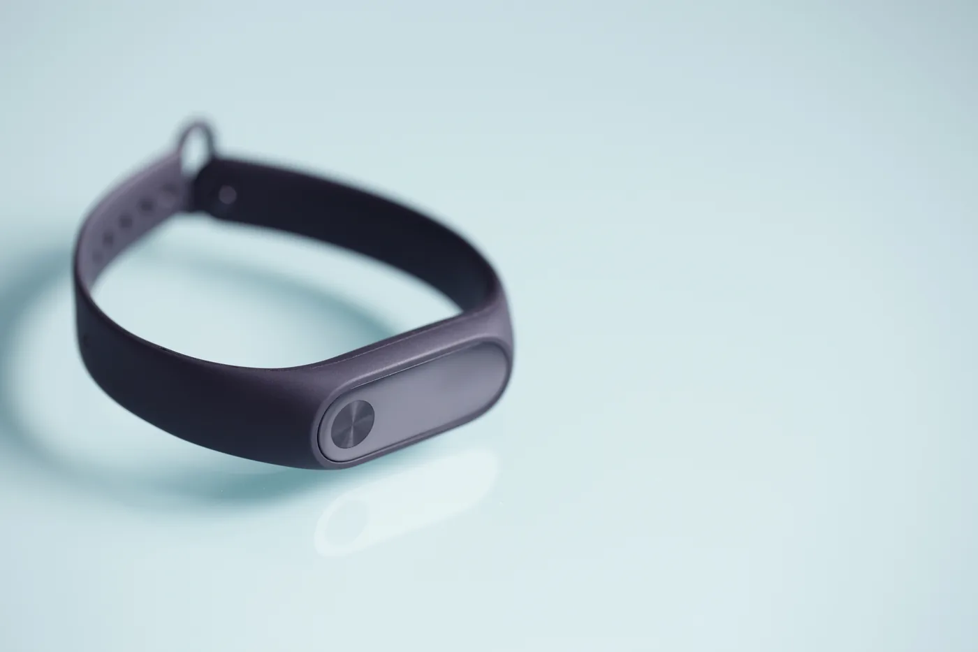 Black fitness tracker wristband on a pale blue surface, close-up product shot with soft reflections.