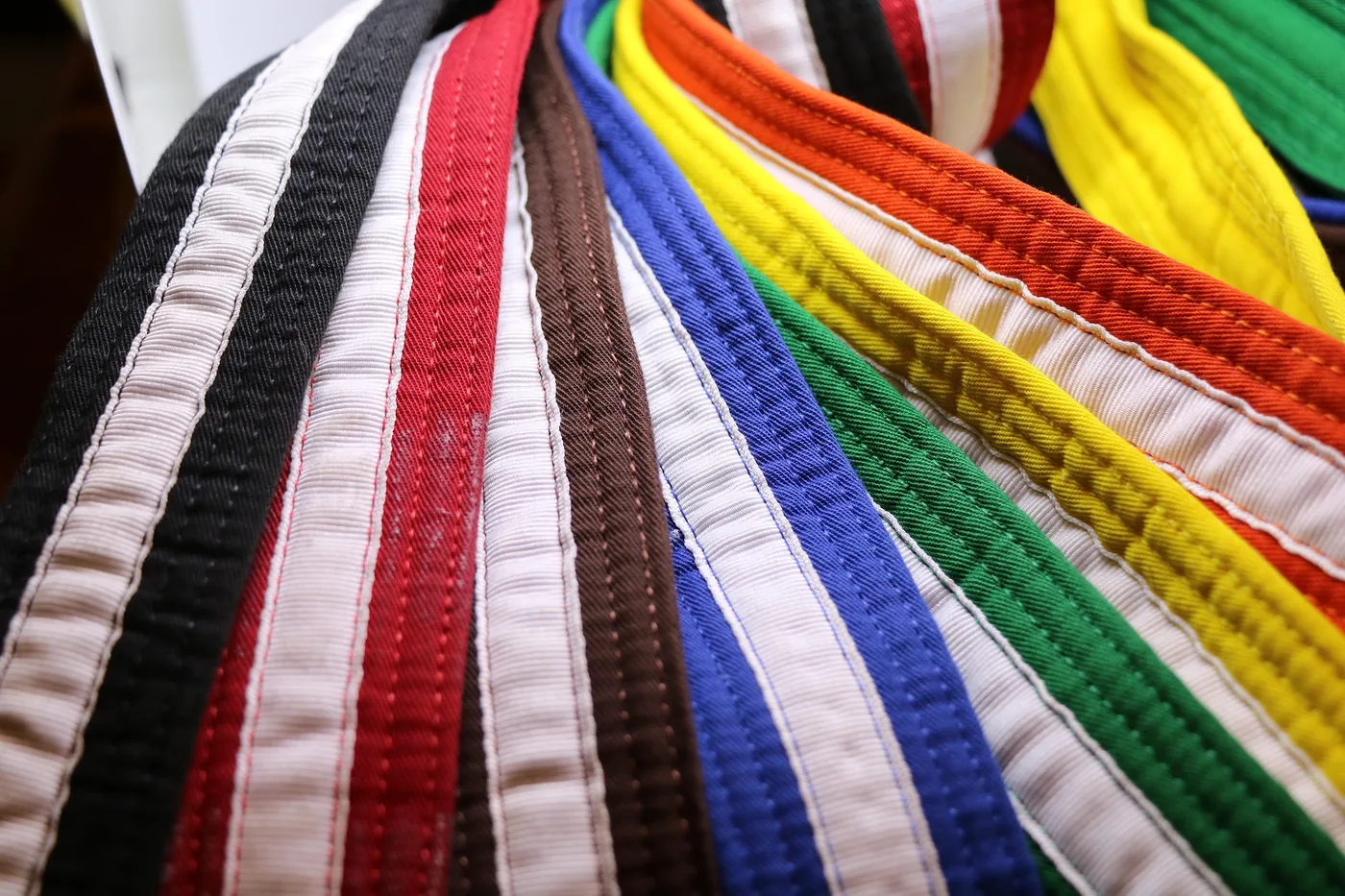 Close-up of colorful woven fabric Karate Belts, fanned out in black, white, red, brown, blue, green, yellow, and orange patterns.