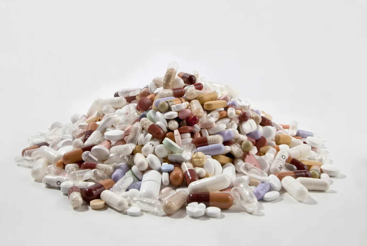 Pile of assorted pills and capsules on a white background, with a few marked tablets visible.
