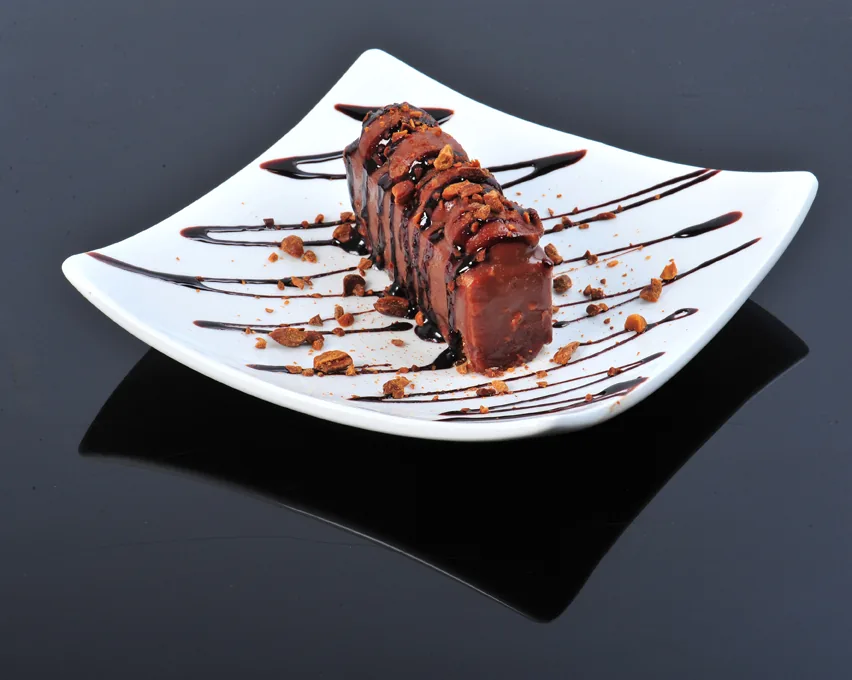 Chocolate dessert loaf drizzled with sauce and crumbs on a white plate against a dark background