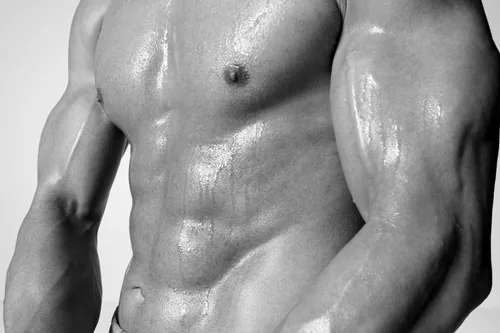 Black-and-white close-up of a muscular shirtless man’s torso and arms, glistening with sweat against a plain background.