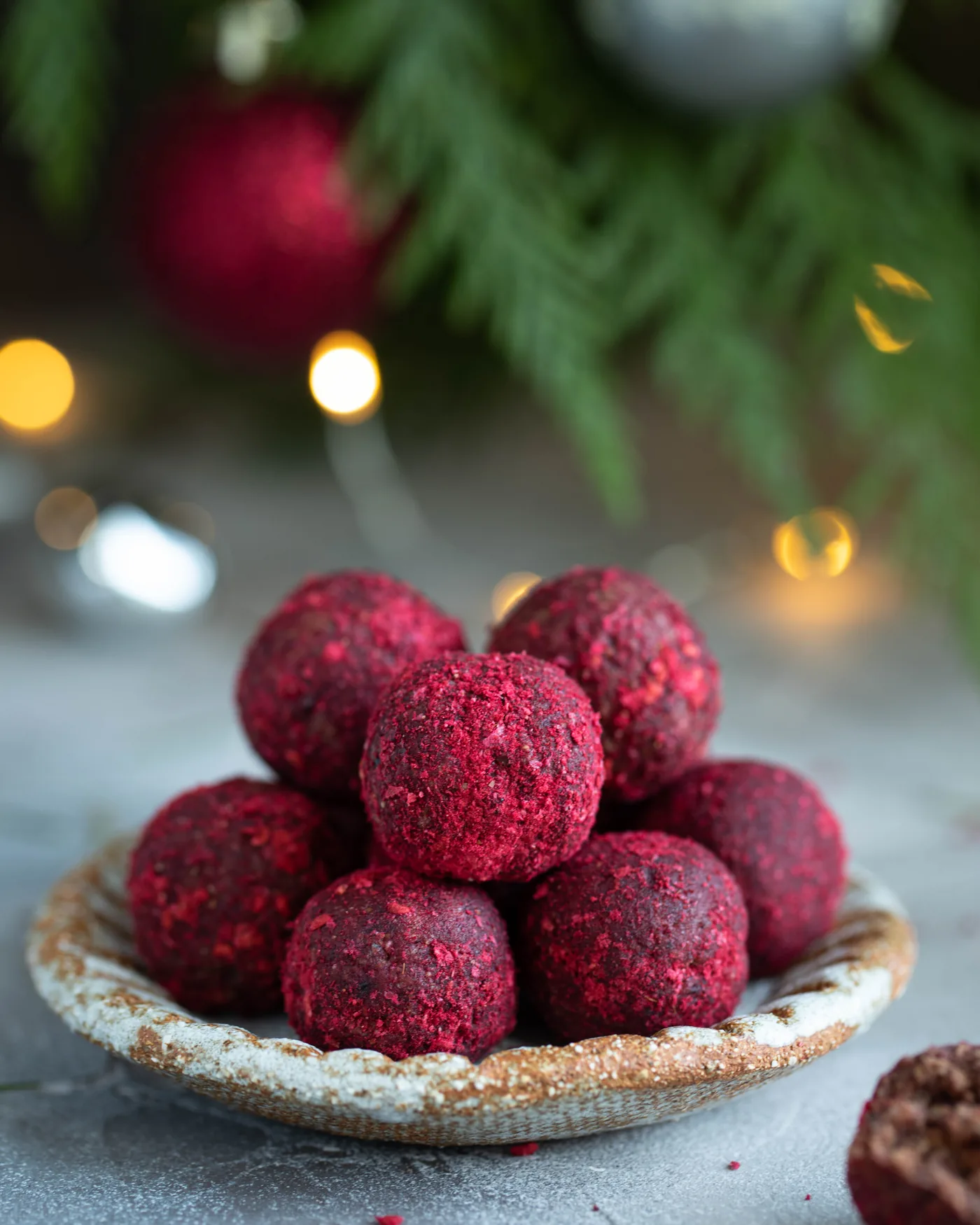 Plate of red beet bliss balls on a rustic dish, with blurred holiday lights and greenery in the background.