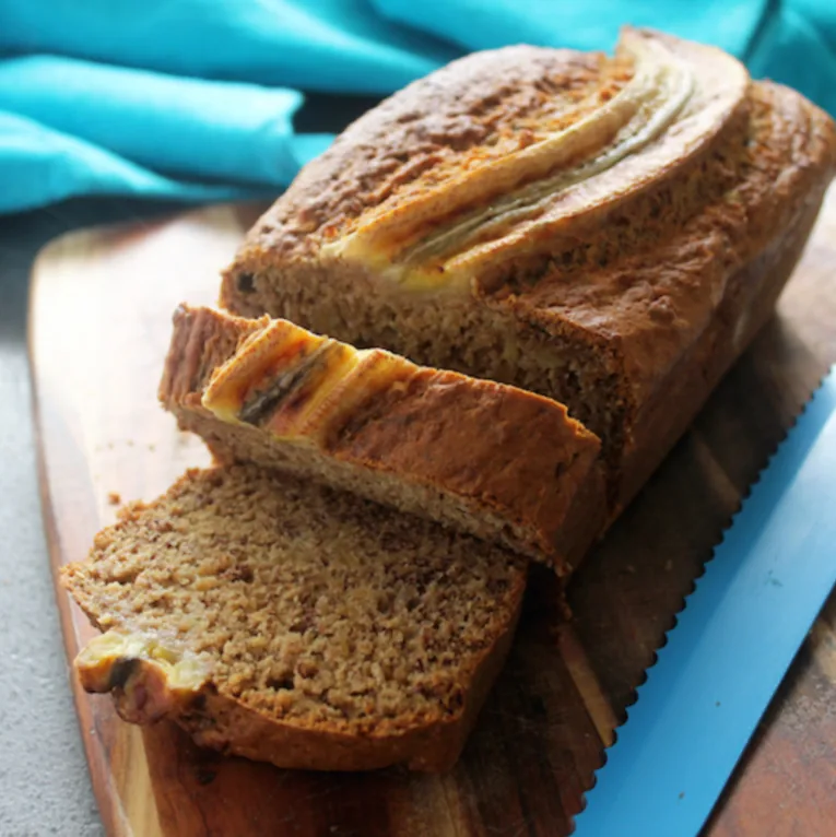 Sliced banana bread loaf on a wooden board, with a blue cloth in the background.
