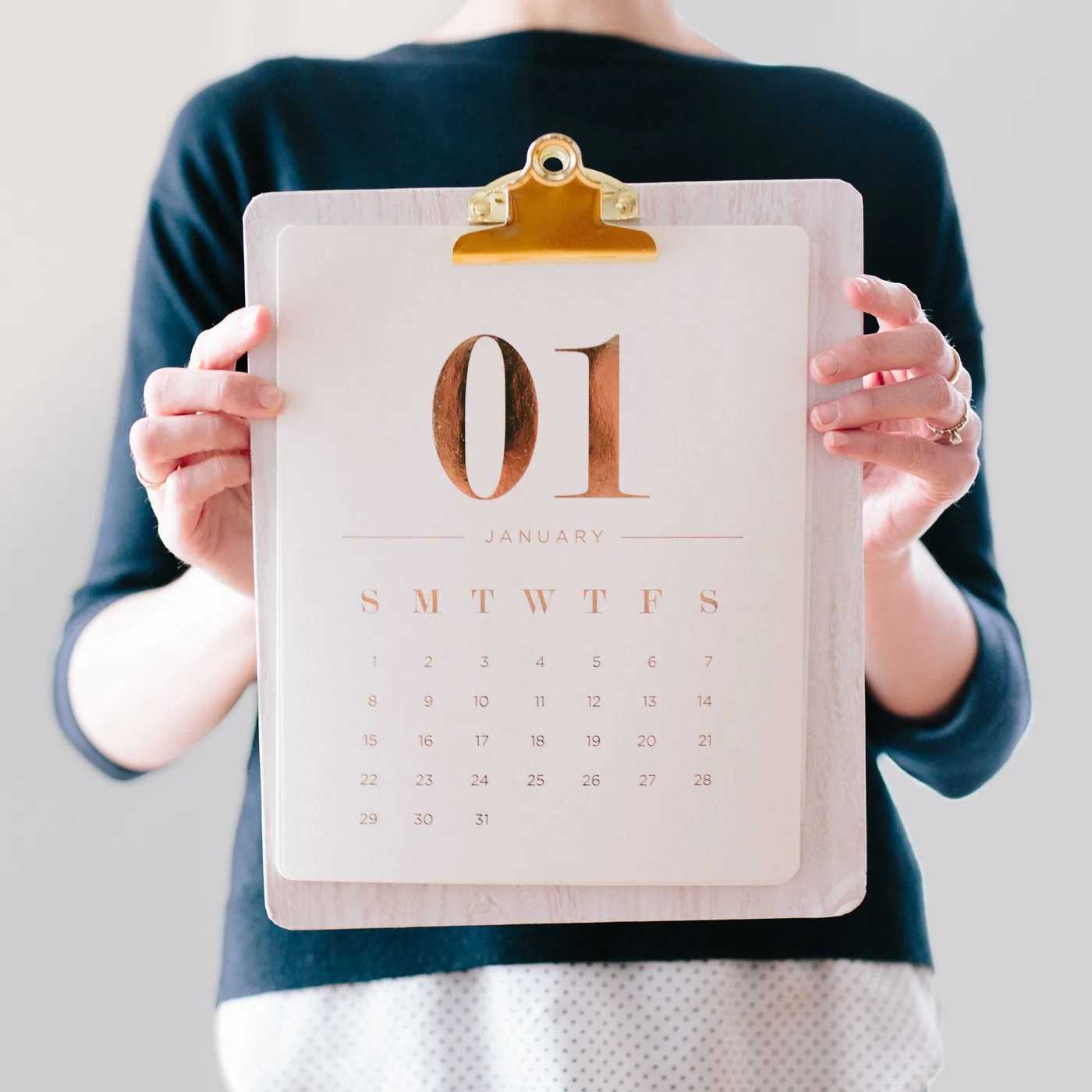 Person holds a January 1 calendar clipboard against a light background, with gold accents and a calm, minimal look.