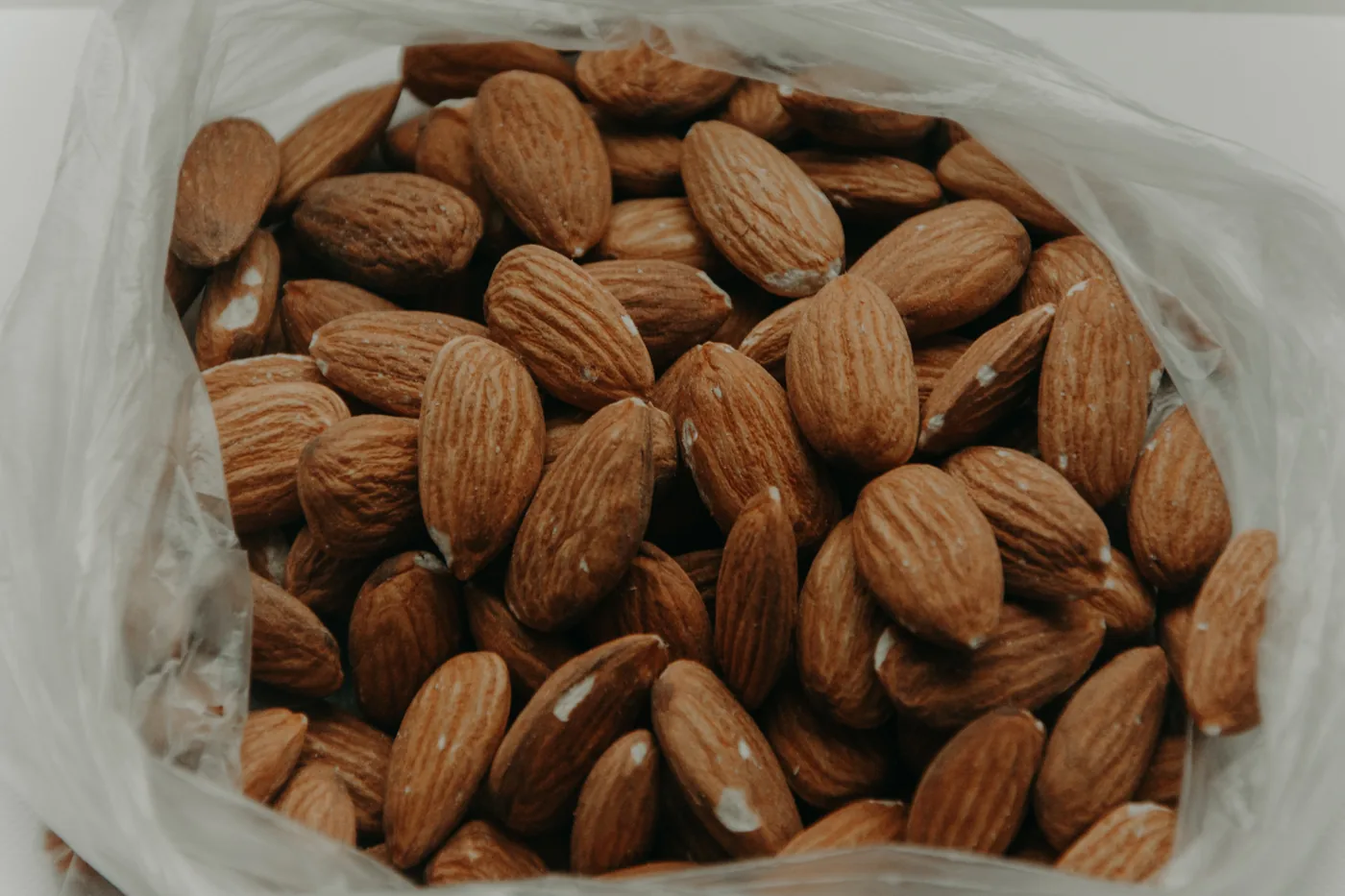 Close-up of a plastic bag filled with brown almonds on a plain light background.