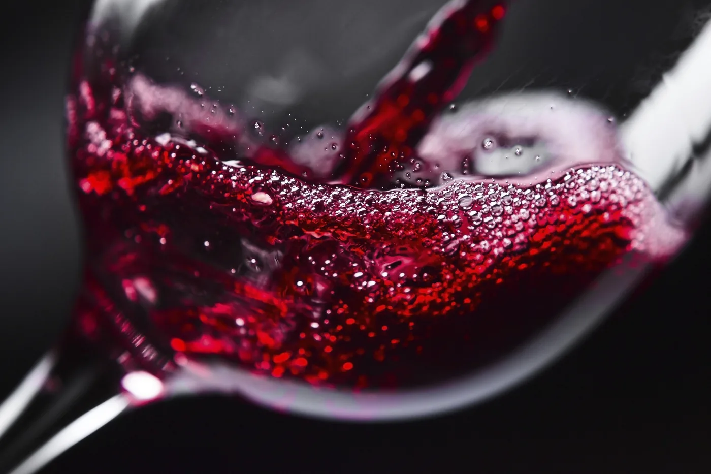 Close-up of red wine pouring into a glass, with bubbles and a dark background, creating a rich, glossy abstract look