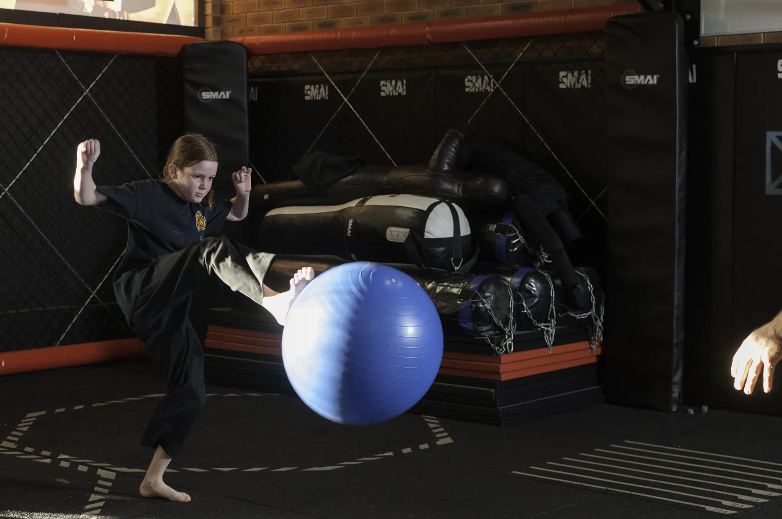 A child kicks a large blue exercise ball during a Little Dragons coordination drill.