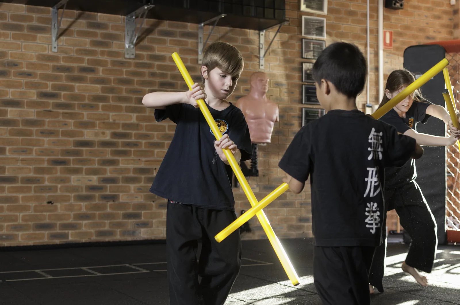 Two Little Dragons students practise together with yellow training sticks.