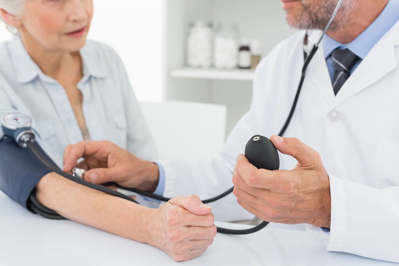 Doctor checks elderly woman's blood pressure with a cuff in a bright clinic, calm medical exam, no visible text