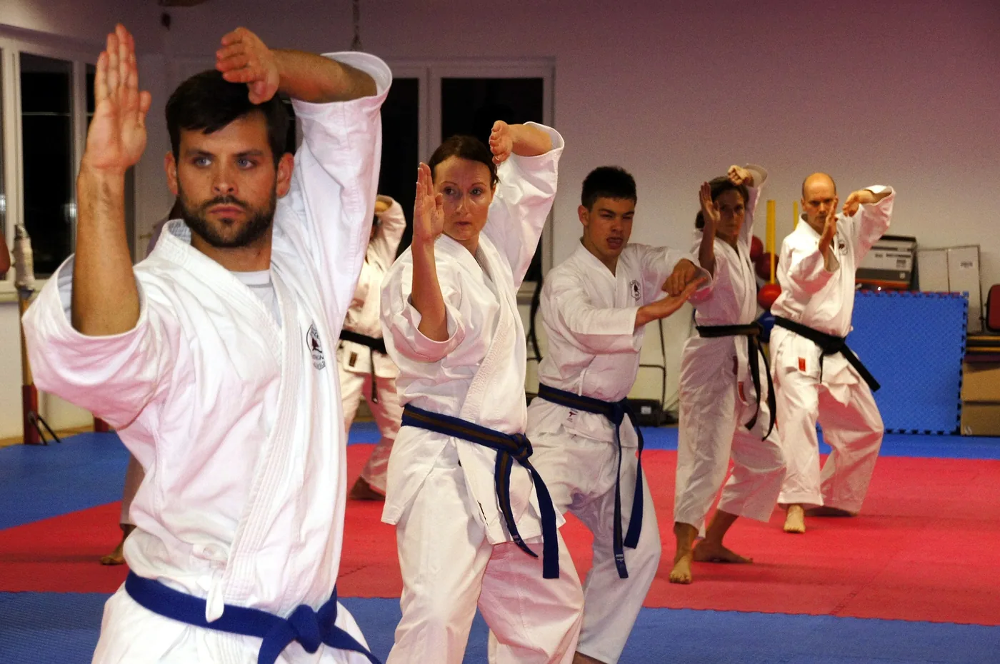 Karate class in white gis performs a kata on red-and-blue mats in a dojo, focused and synchronized.