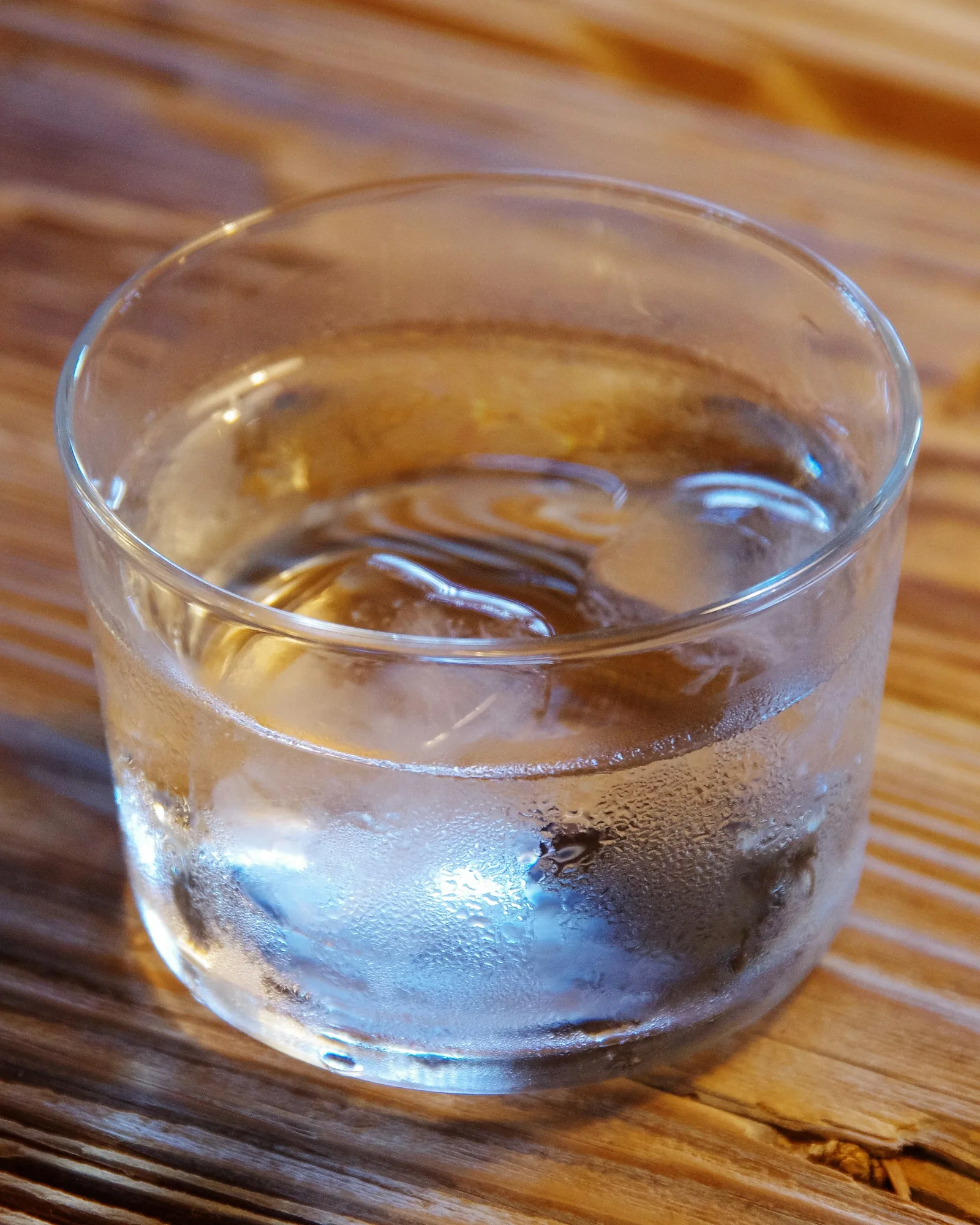 A glass of cold water with ice on a wooden table.