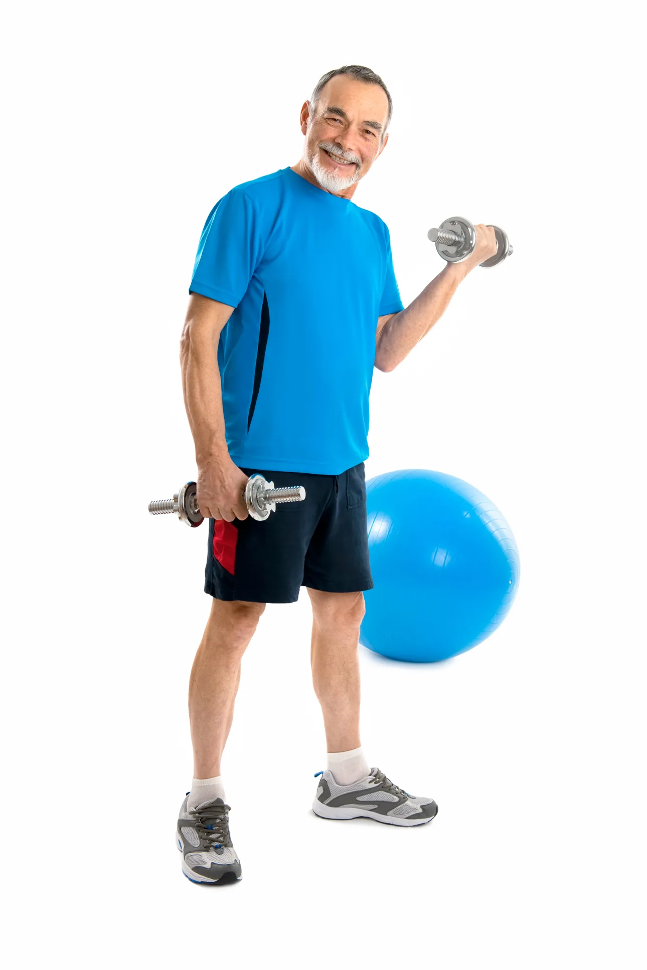 Smiling older man in a blue workout shirt lifting dumbbells beside a blue exercise ball on a white studio background.