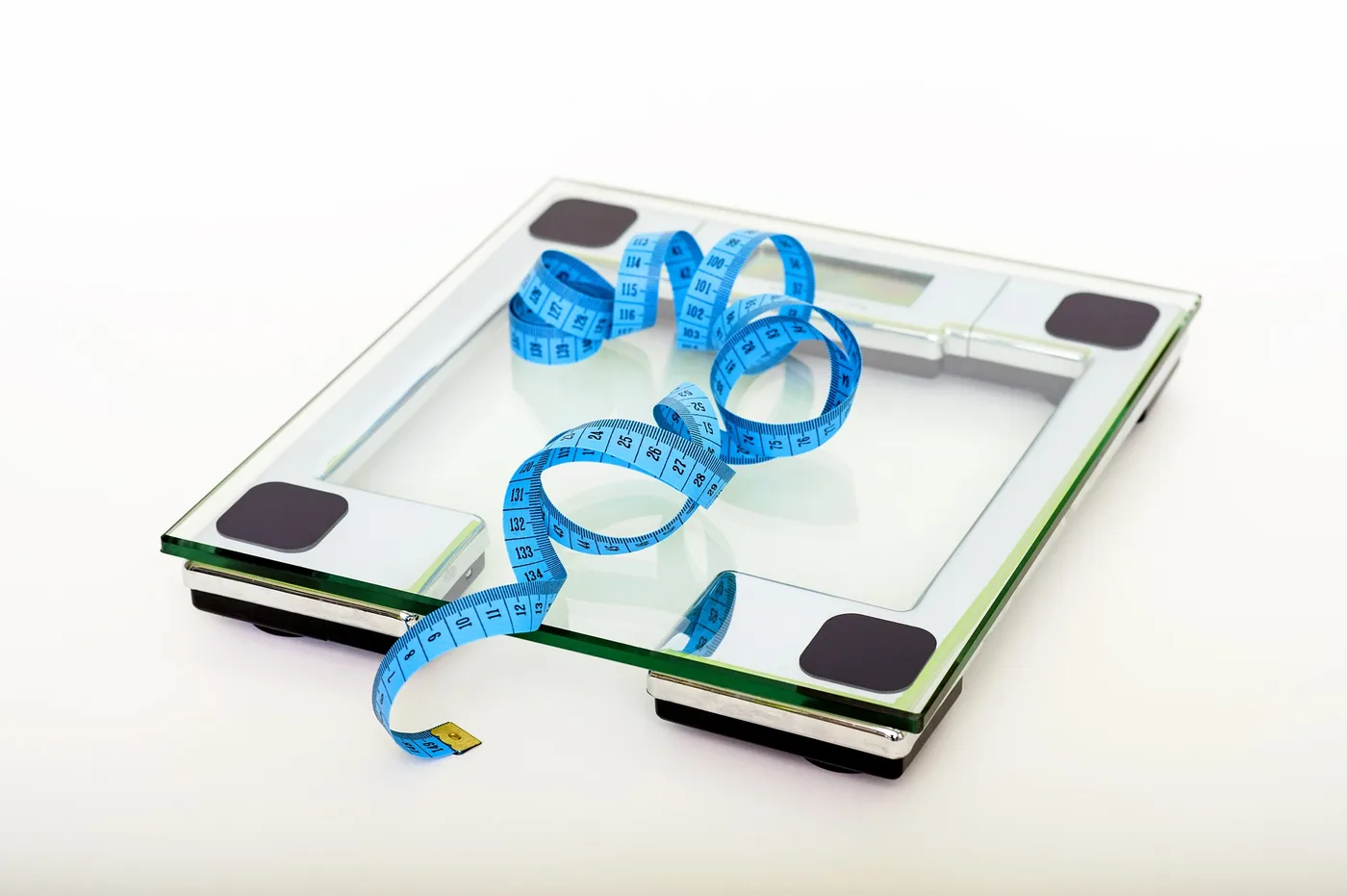 Blue measuring tape curled on a glass bathroom scale against a white background