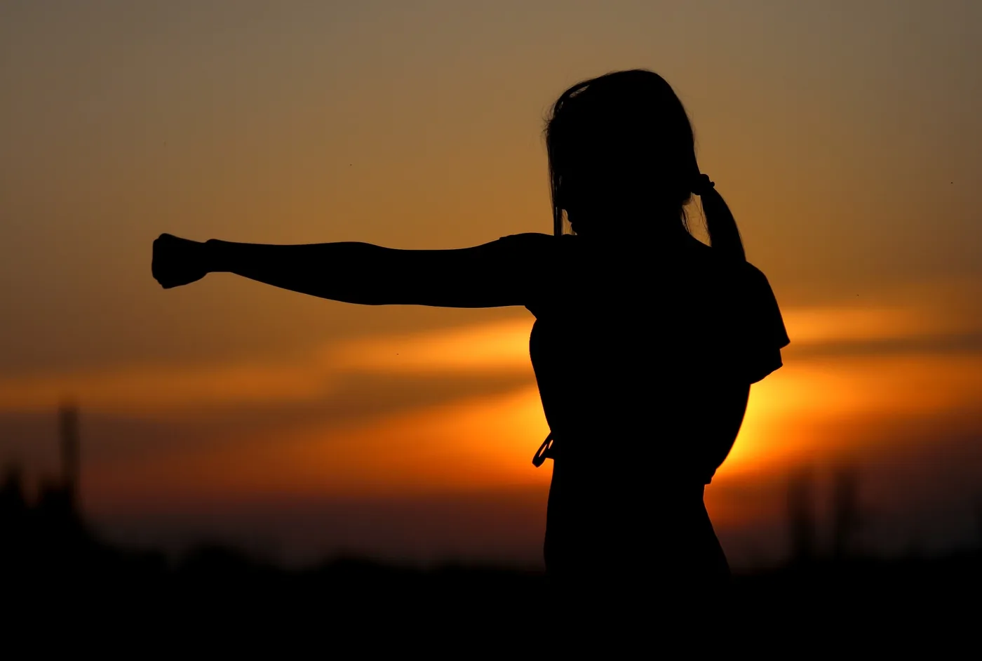 Silhouette of a girl with one arm extended against a glowing orange sunset sky, calm and energetic mood.