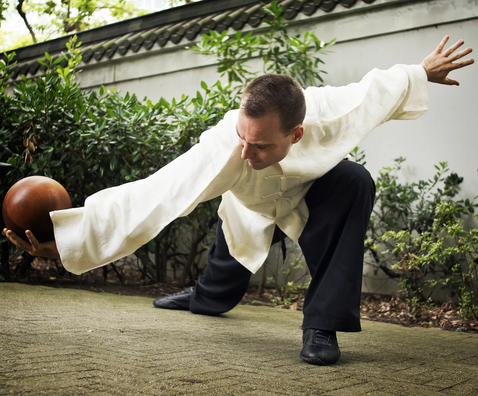 Taiji Ball Qigong: a deep lunge holding a wooden ball, arms spread wide.