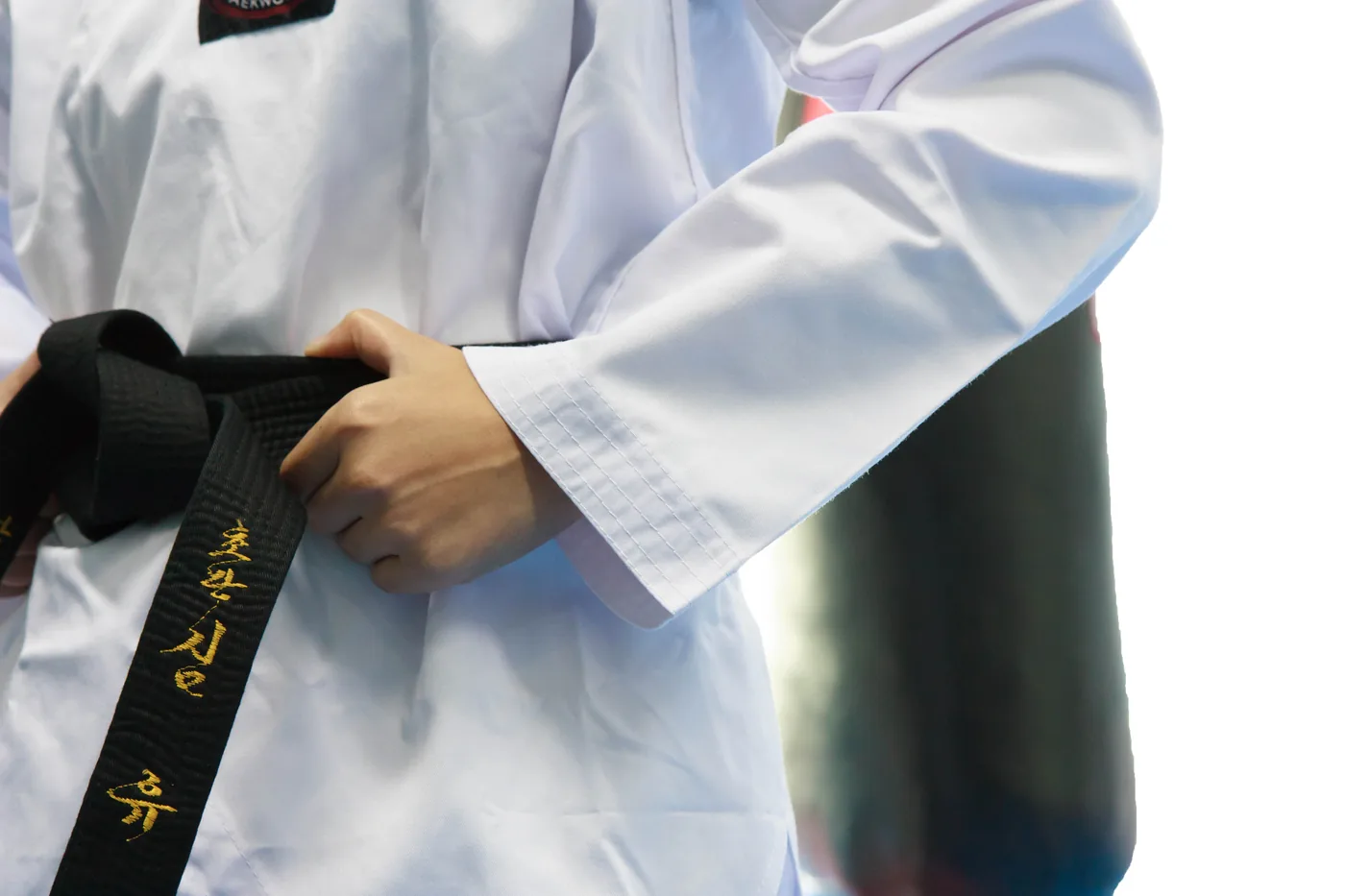 Close-up of a taekwondo student tying a black belt on a white dobok, gold lettering visible, focused training mood