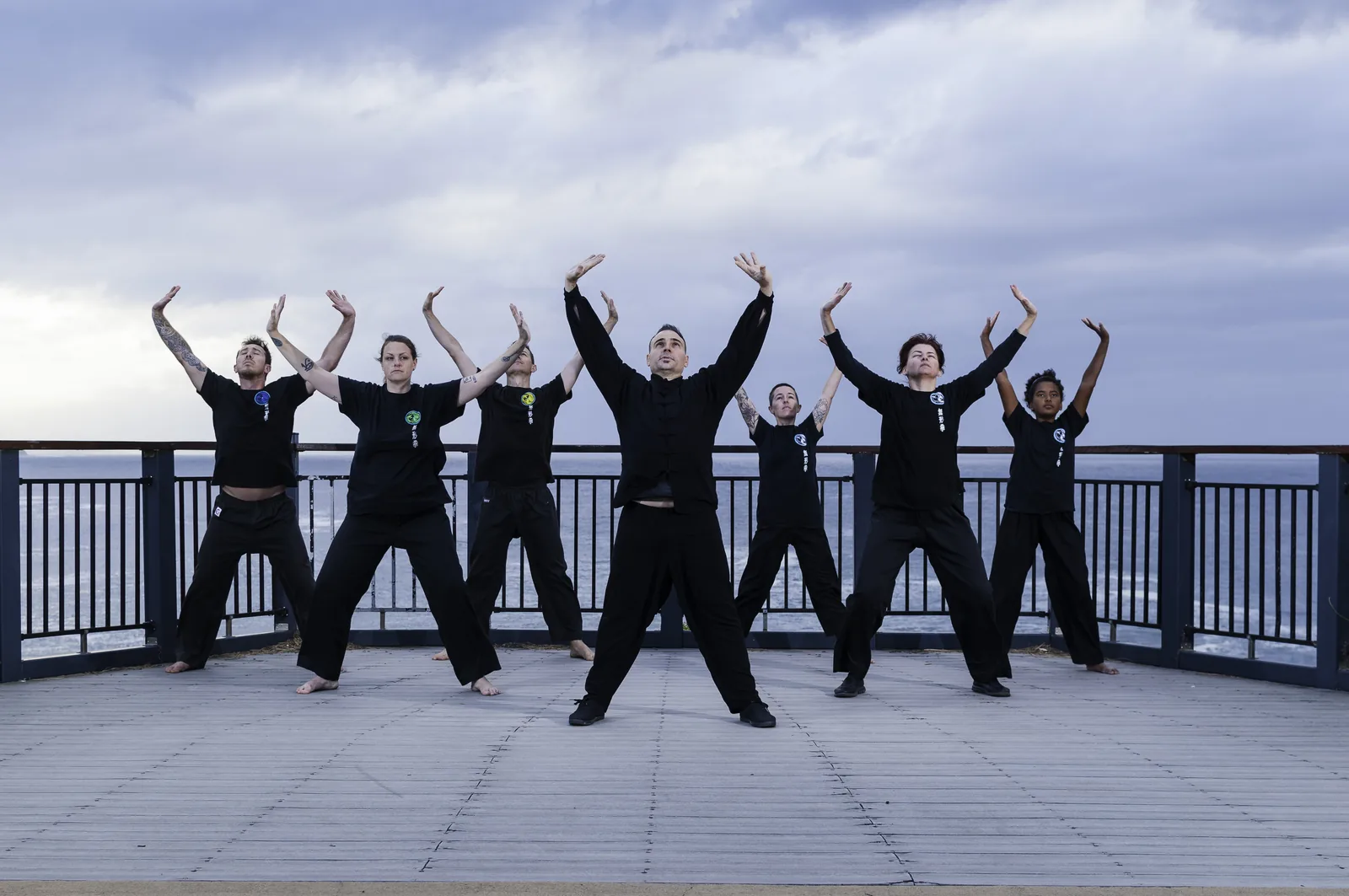 Wu Xing Dao students raise their arms together in group Qigong by the sea.