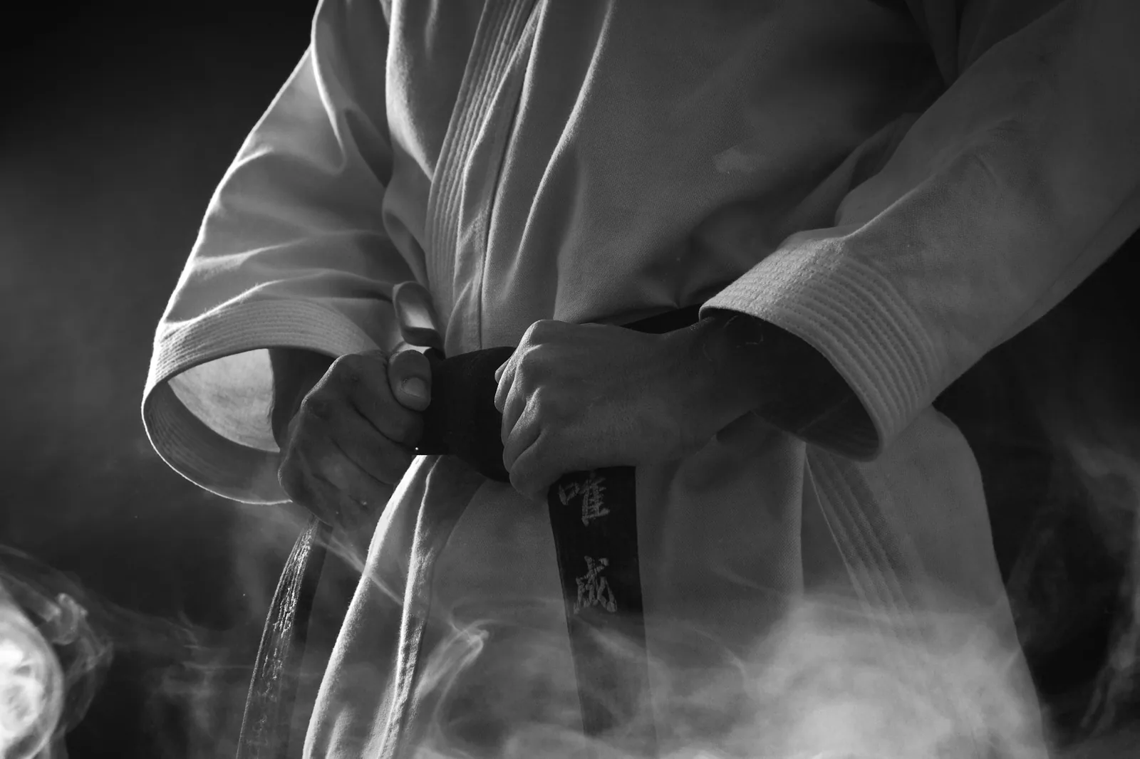 A martial artist tightens a black belt over a white gi.