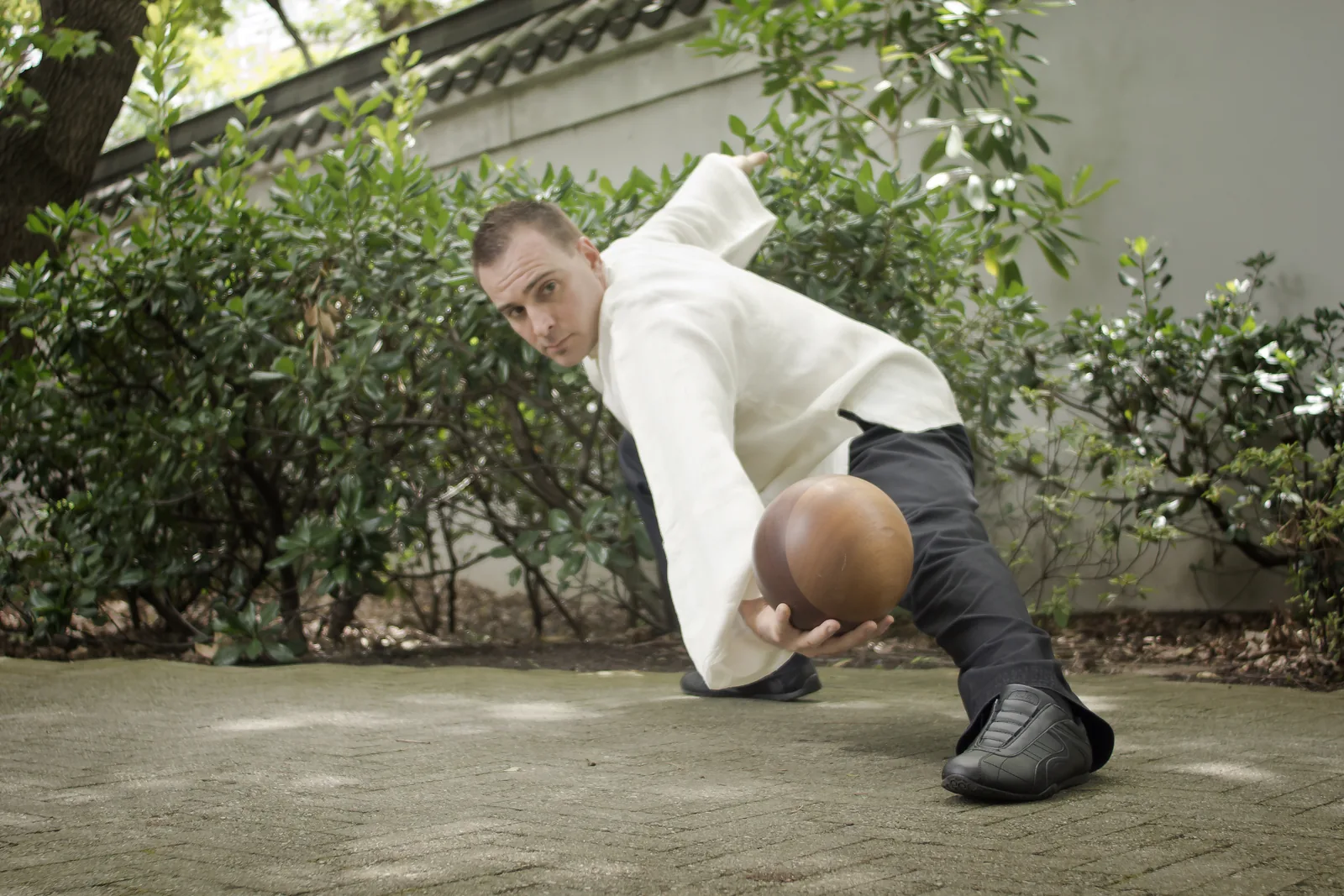 Taiji Ball Qigong in a garden: a wide stance holding a wooden ball.