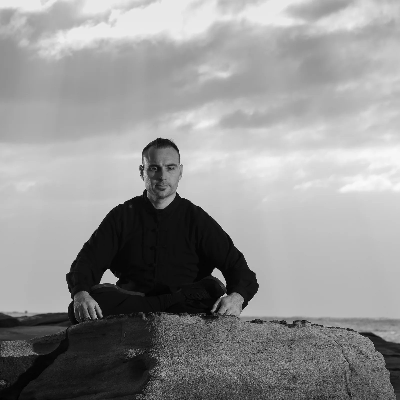 Seated Qigong on a sea rock to recover after training, in black and white.