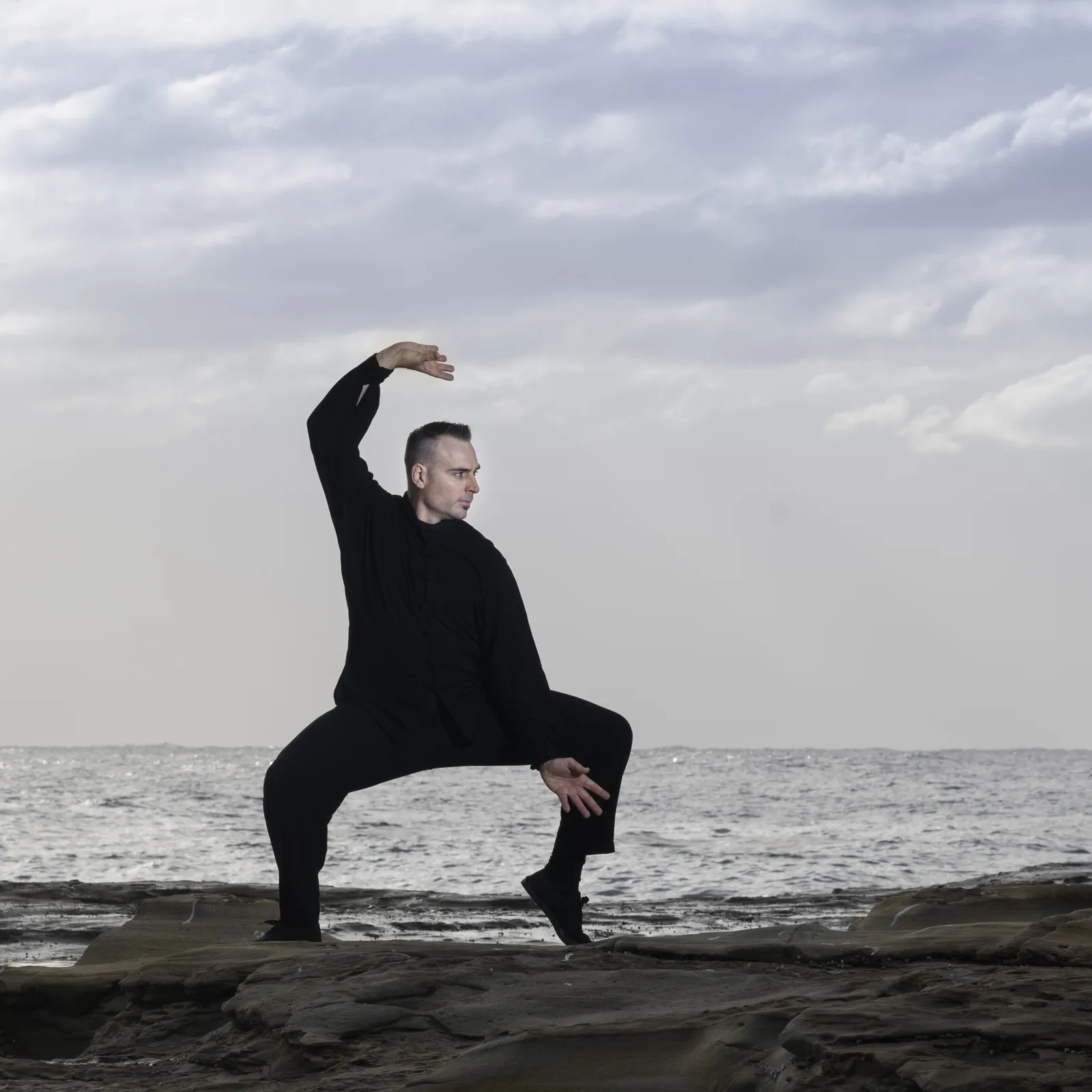 A Qigong stance on the rocks at Terrigal with the ocean behind.