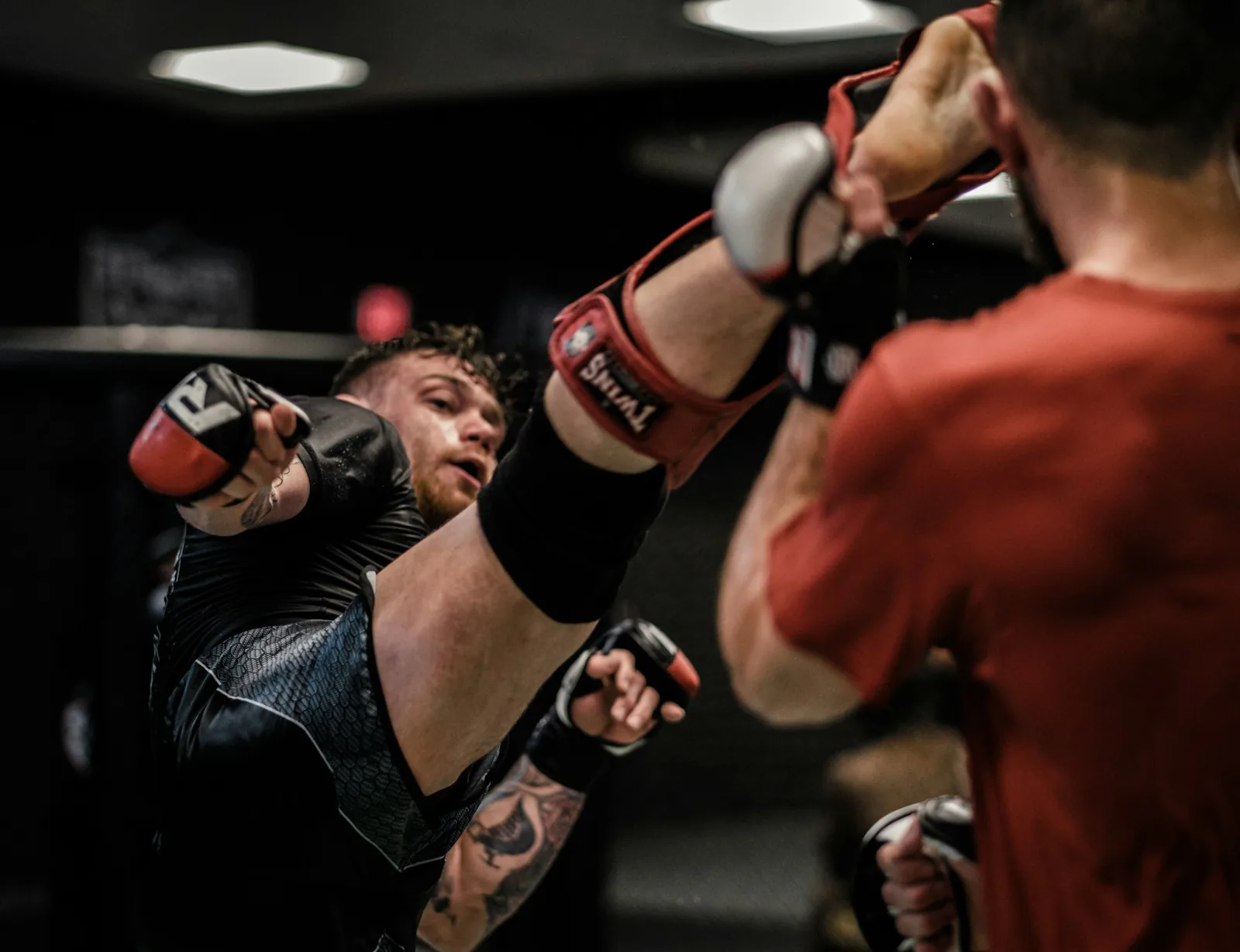 An MMA fighter lands a kick on an opponent in red gloves.