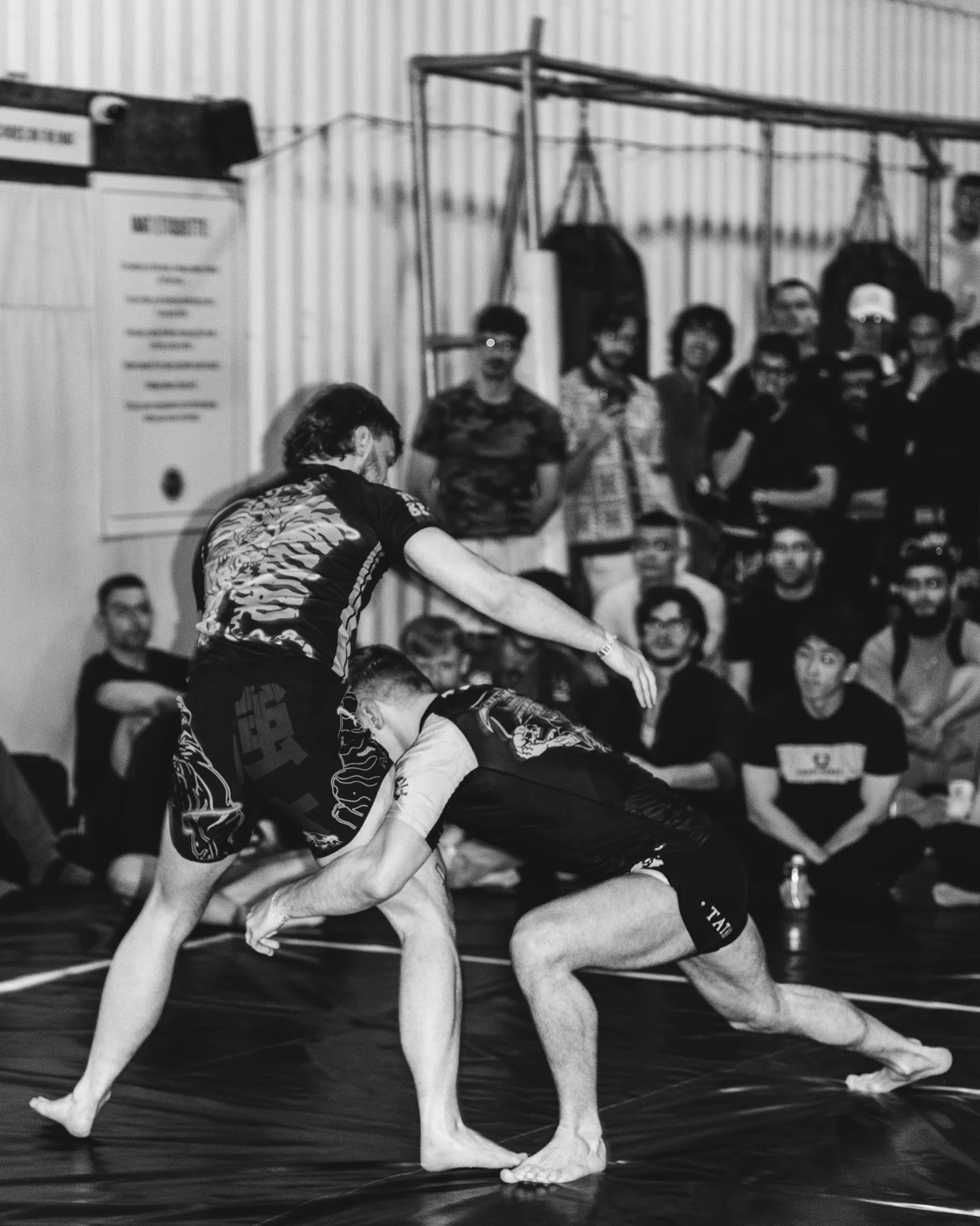 Two men grappling on a mat in a training facility.