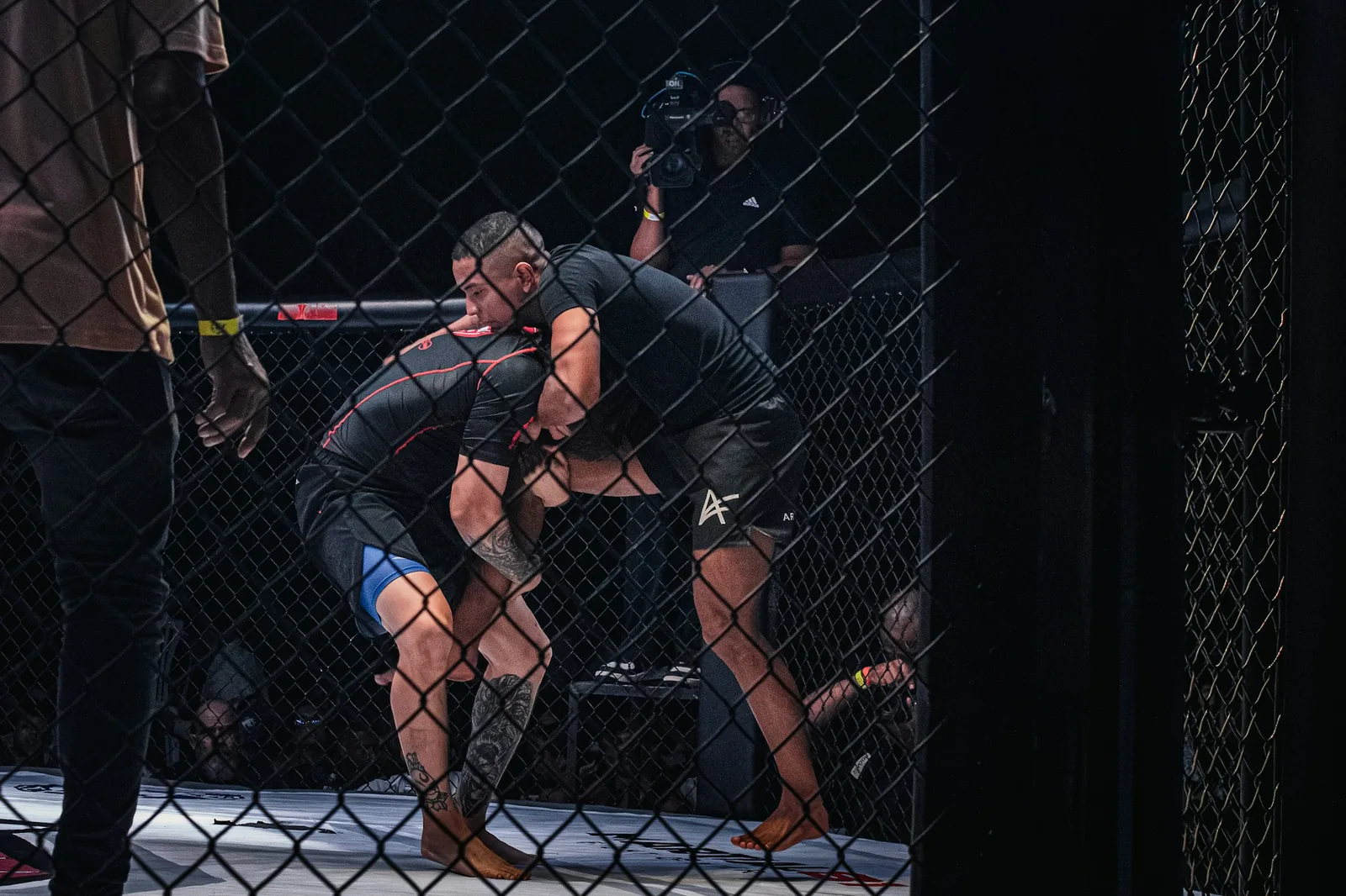 Two fighters grappling against the cage wall.