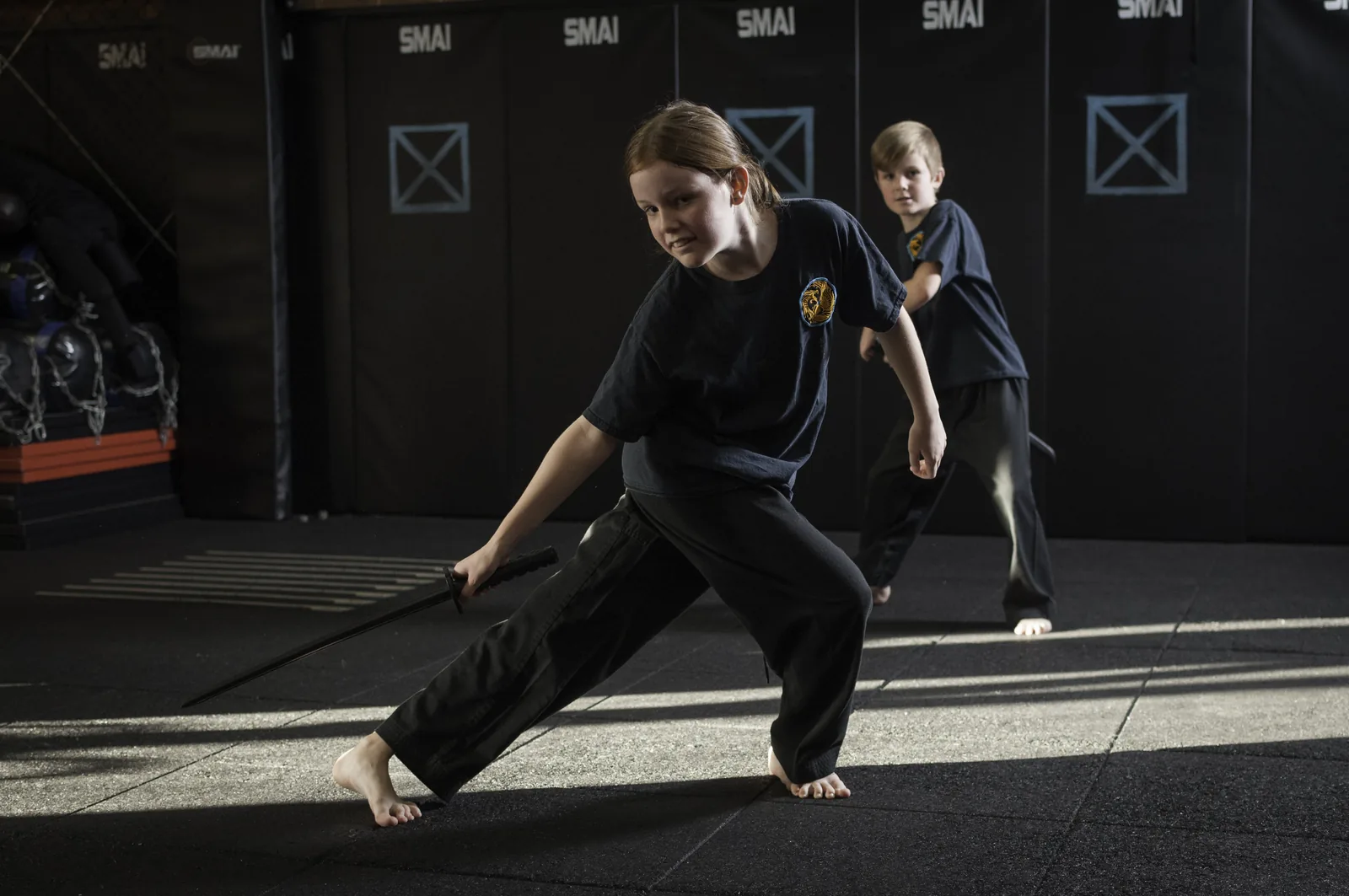 A young student practises a long, low stance with a training sword.